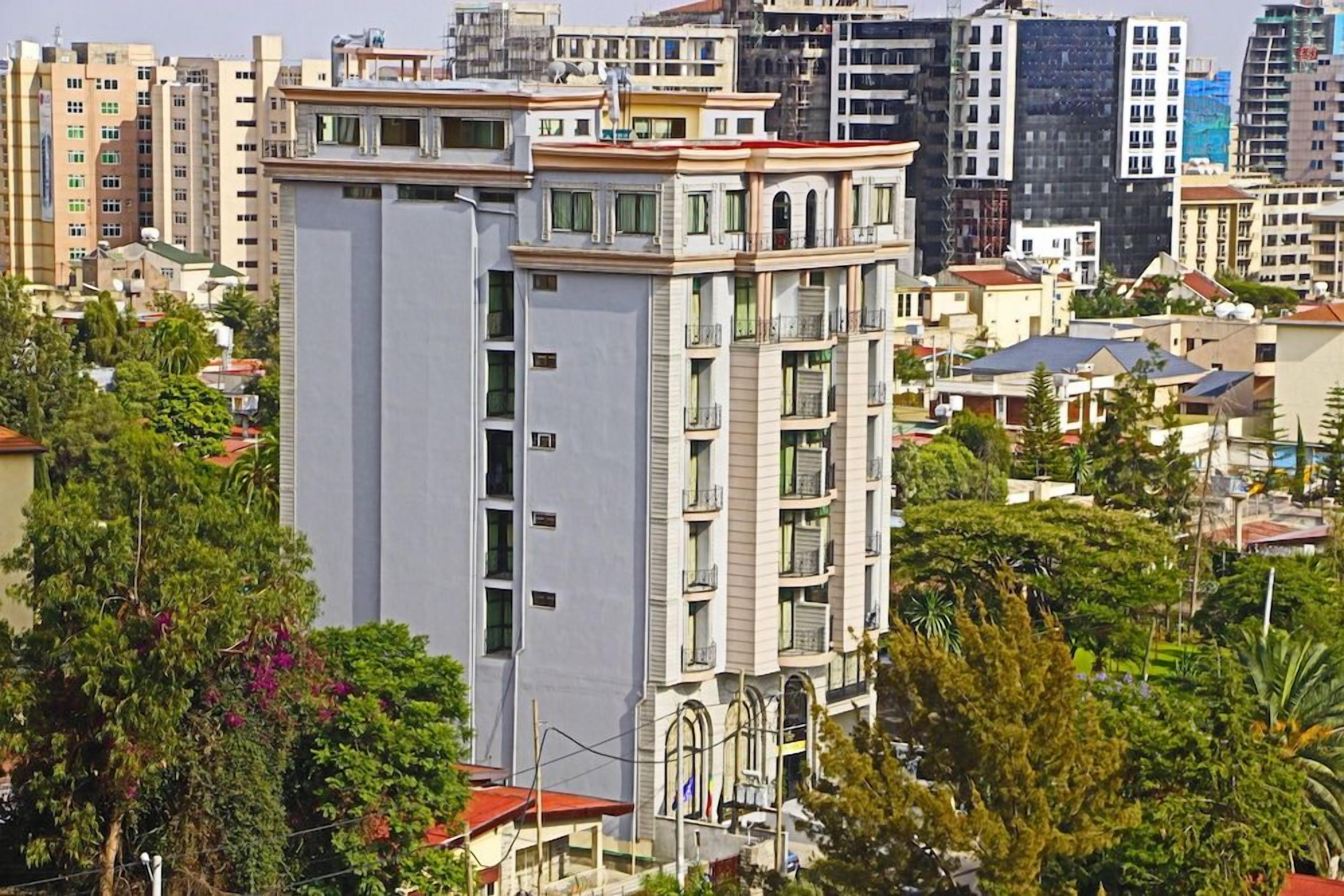 A multi-story building with balconies, surrounded by other residential buildings and greenery.