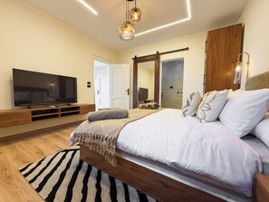 A modern bedroom with a large bed, a flat-screen TV, wooden flooring, and a striped rug. - Private Jacuzzi Escape  Romantic & Luxurious (Cairo Governorate)
