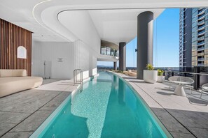 Ein moderner Innenpoolbereich mit einem langen rechteckigen Pool, Liegebereich und Blick auf die Stadtlandschaft.