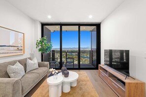A modern living room with a sofa, coffee table, TV, and a balcony with a city view. - CASSA CASINO TOWER 2 - Brand New Premium Residence Managed by The Cassa (Broadbeach)