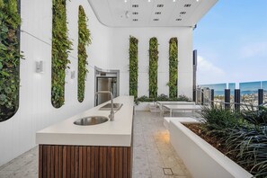 Un área moderna de cocina al aire libre con pileta integrada, rodeada de jardines verticales y vista a la ciudad.
