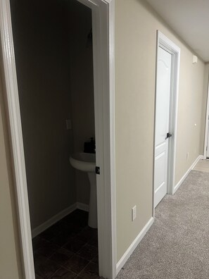 Un couloir avec des toilettes, un lavabo et une porte.