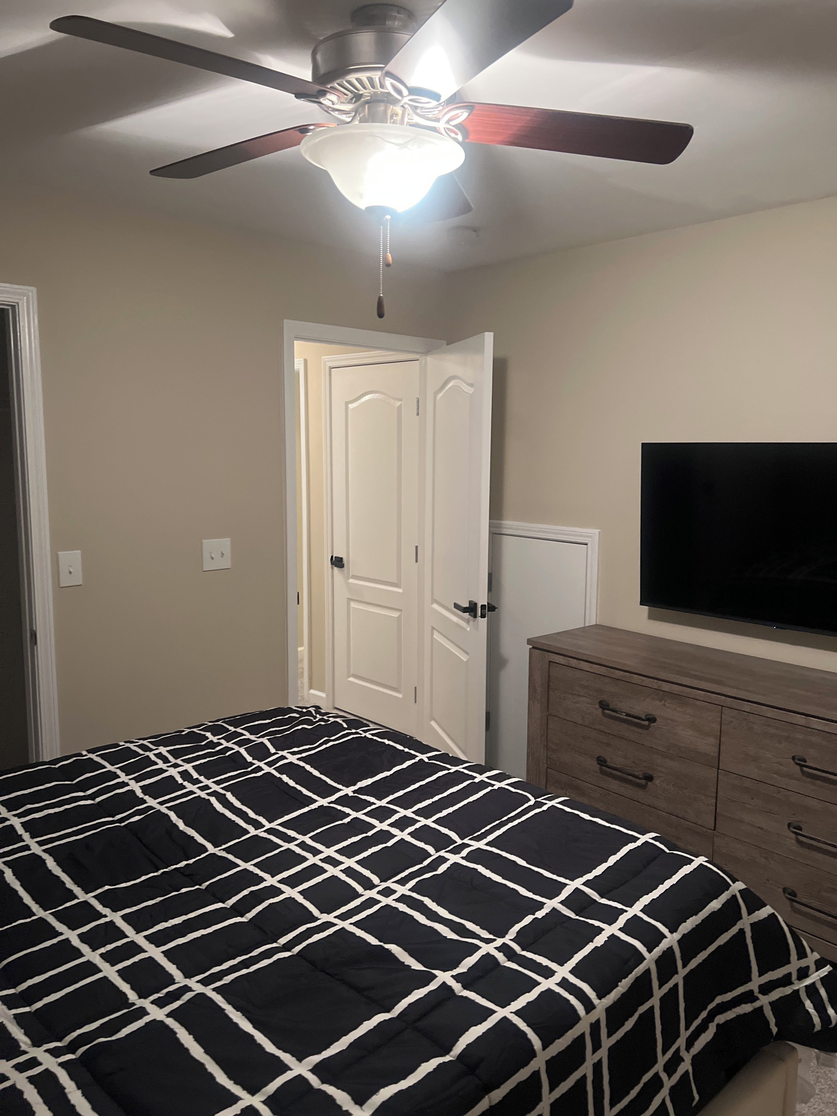 Una camera da letto con un letto, una ventola a soffitto, una televisione e un comò.