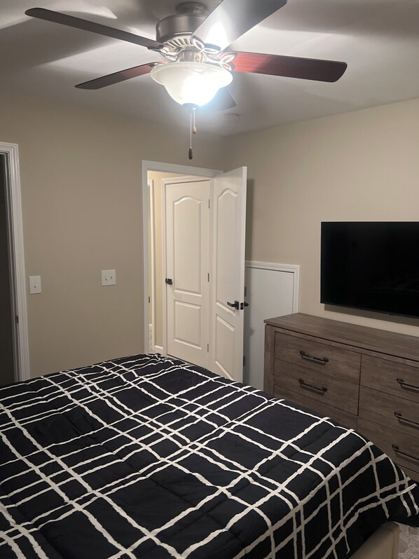 A bedroom with a bed, a ceiling fan, a television, and a dresser.