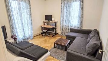 Un salon comprenant un canapé, une petite table, un téléviseur et un bureau avec une chaise.