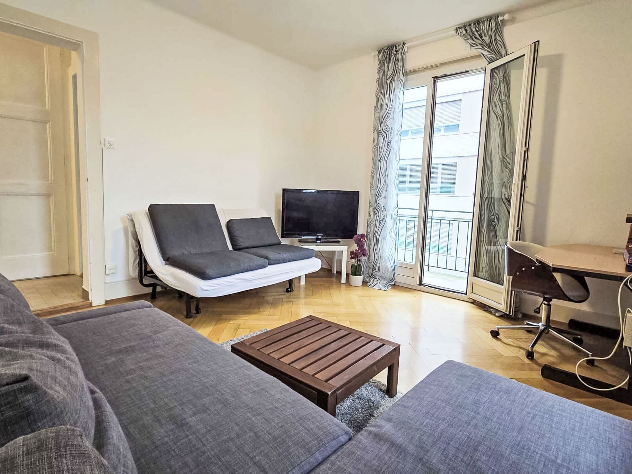 A living room with a sofa, a coffee table, a TV, and a desk with a chair.