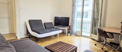 A living room with a sofa, a coffee table, a TV, and a desk with a chair.