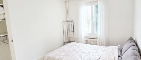 A bedroom with a bed, a radiator, a window with curtains, and a door.