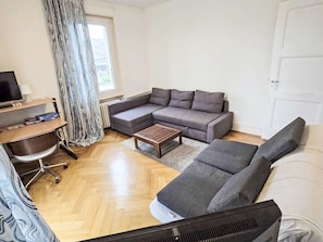 A modern living room with a sectional sofa, a wooden coffee table, a TV, and a desk with a chair.