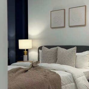 Ein modernes Schlafzimmer mit einem Bett, Kissen, einer Nachttischlampe und zwei gerahmten Wandbildern.