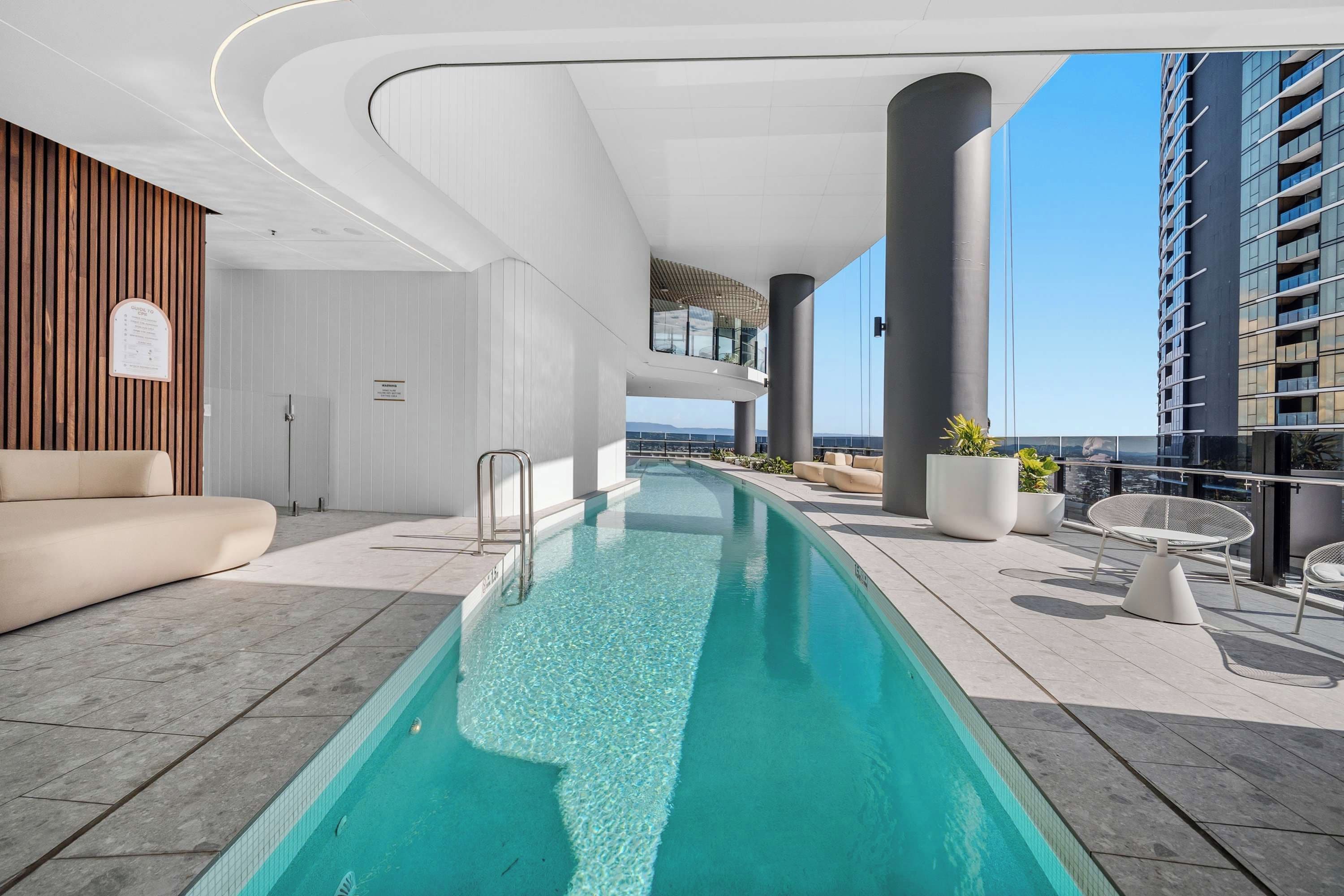 Ett modernt inomhuspoolområde med en lång, rektangulär pool, bekväma sittplatser och utsikt över stadsbilden.
