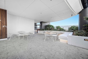 An outdoor seating area with white chairs and a white sofa, surrounded by plants and a view of the city. - CASSA CASINO TOWER 2 - Brand New Premium Residence Managed by The Cassa (Broadbeach)