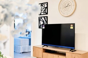 Ein modernes Wohnzimmer mit einem Flachbildfernseher auf einem Holzständer, einer Wanduhr und abstrakten Kunstwerken.