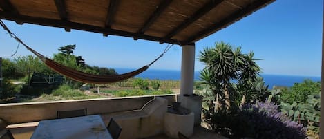 Un espacio al aire libre techado con mesa y sillas, una hamaca y vistas al océano.