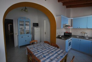 Una cocina con armarios azules, una mesa de comedor con mantel estampado y un refrigerador.
