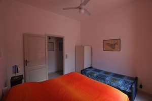 Un dormitorio con cama, armario, ventilador de techo, puerta y un mapa colgado en la pared.