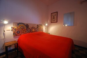 Una habitación con una cama, un tapiz de pared, un cuadro enmarcado y un espejo.