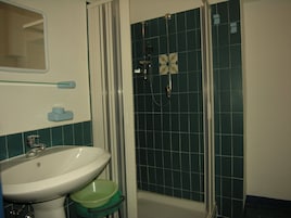Un baño con un lavabo blanco, una pileta verde, una ducha con puerta de vidrio y un espejo sobre el lavabo.