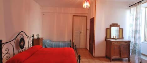 A bedroom with a bed, a dresser, a mirror, and a door leading to another room.