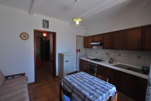 Cocina compacta con armarios de madera, un refrigerador, una estufa y una mesa de comedor con mantel estampado.