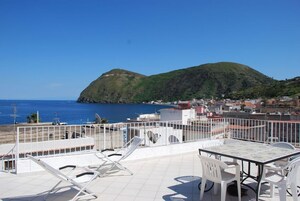 Una terraza con mesa y sillas, con vistas a un pueblo costero y una colina.