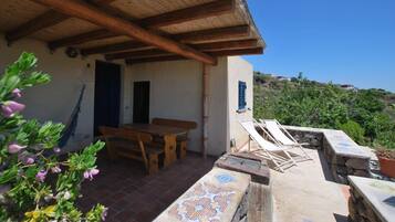 Un patio al aire libre cubierto con una mesa de madera y bancos, una pared de piedra con un diseño de azulejos y vistas a una colina.