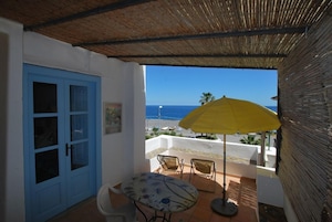 Un balcón con mesa y sillas, un paraguas amarillo y vista al mar.