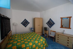 Un dormitorio con cama, armario, silla, cómoda, televisor y decoración en las paredes.