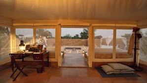 Quarto com tenda, uma escrivaninha, cadeira e vista para área externa com muro de pedra e tenda branca.