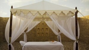Cama com dossel, com a parede de pedra e janelas em arco ao fundo.