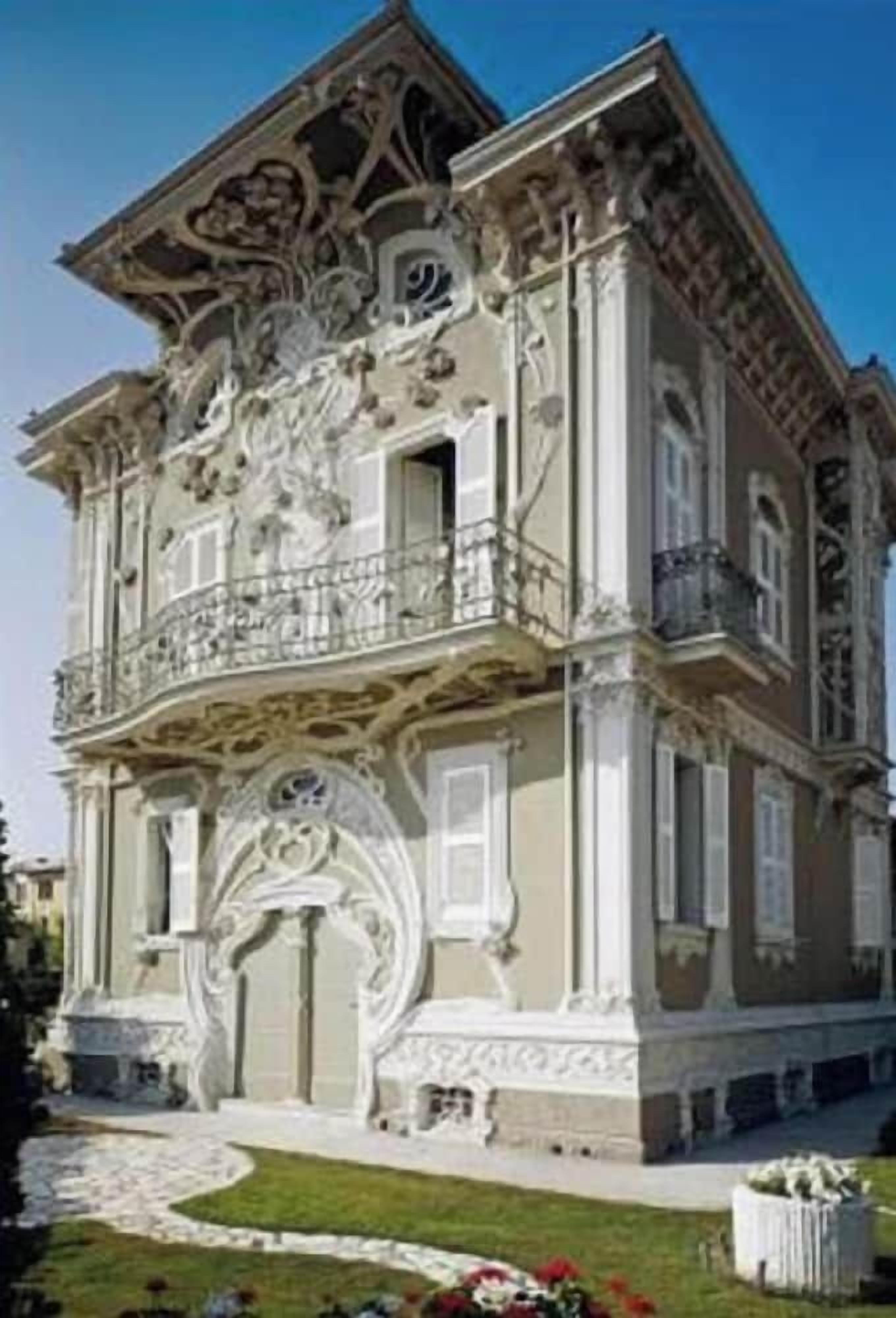 Een historisch pand met weelderige architectonische versieringen, een balkon en een verzorgde tuin.
