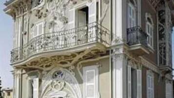 Een historisch pand met weelderige architectonische versieringen, een balkon en een verzorgde tuin.