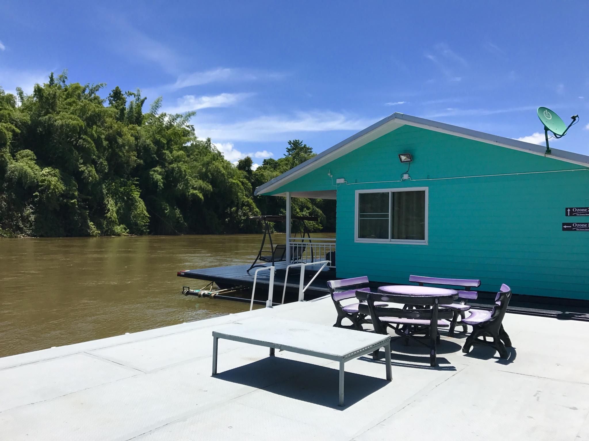 Una pequeña cabaña azul con un muelle, una mesa y sillas, con vistas a un río.