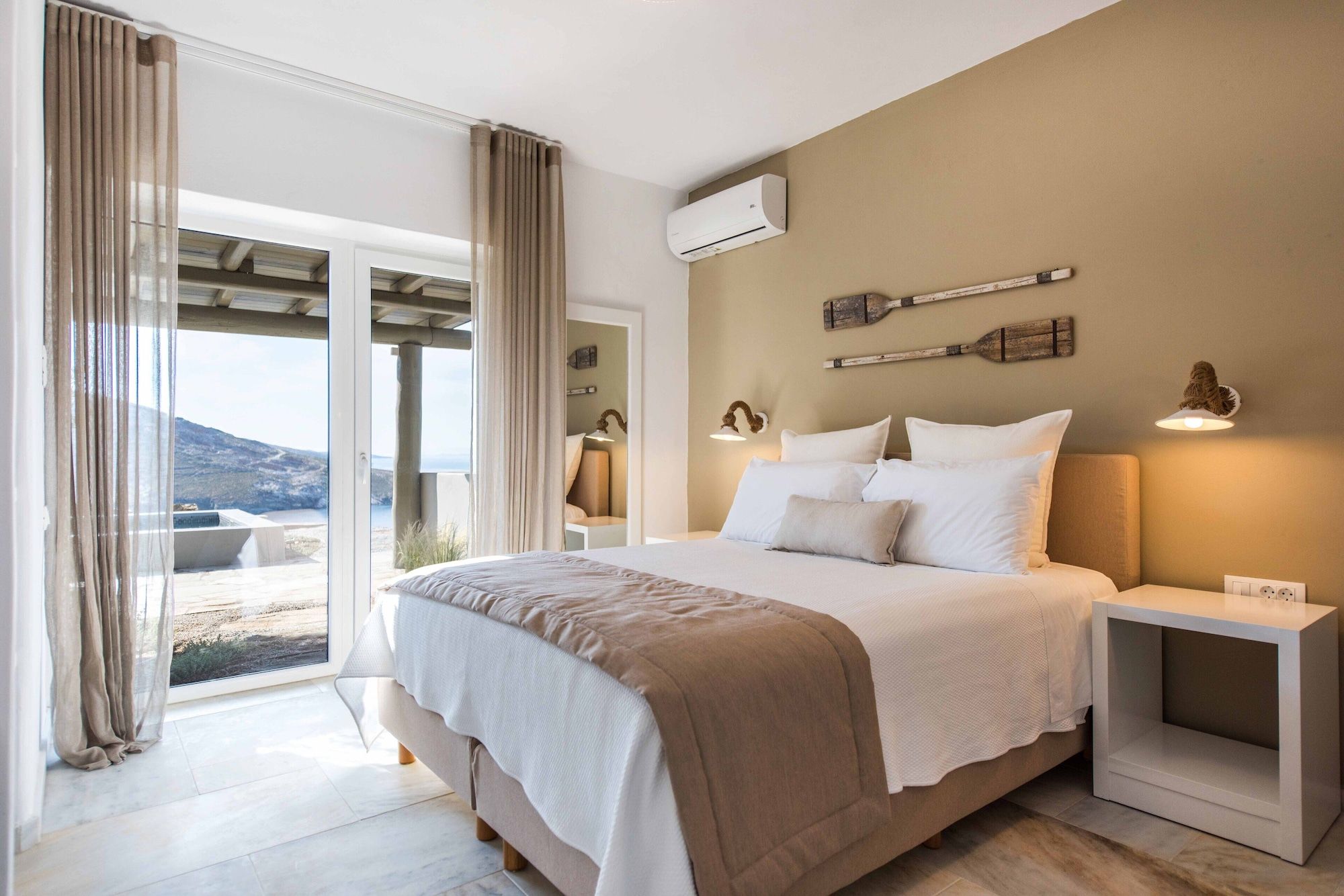 Ein Schlafzimmer mit Bett, Nachttischen, einer Klimaanlage und Blick ins Freie.