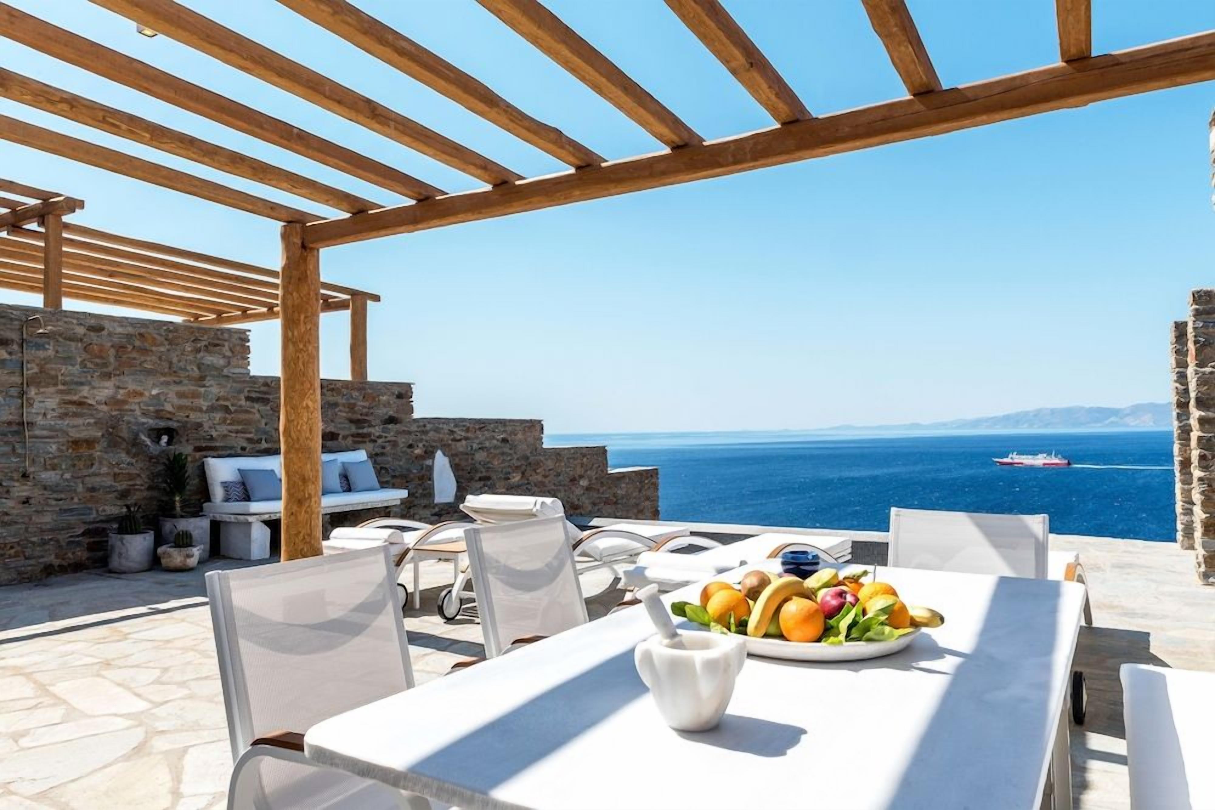 Ein Essbereich im Freien mit Steinsäulen, einer Holzw pergola und Blick aufs Meer.