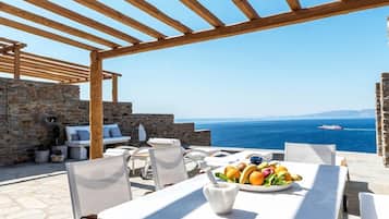 Ein Essbereich im Freien mit Steinsäulen, einer Holzw pergola und Blick aufs Meer.