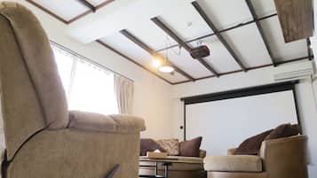 A living room with a large recliner, two armchairs, a coffee table, and a ceiling-mounted projector.