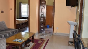 A living room with a sofa, a coffee table, and a television. There is a door leading to a bedroom. - Shine Nepal (Kathmandu)