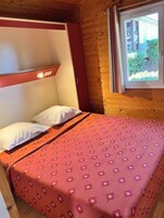 Un lit simple avec une couvre-lit à motifs, une tête de lit et une fenêtre donnant sur un paysage verdoyant.