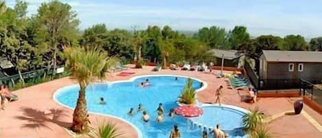A swimming pool area with multiple pools, surrounded by palm trees and lounge chairs.