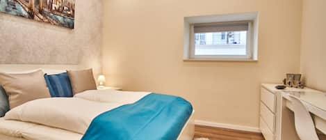 A bedroom with a bed, a desk, a window, and a painting on the wall.