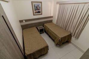 Une chambre avec deux lits, une petite table, un tableau au mur et une fenêtre avec des rideaux.