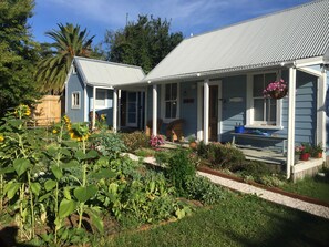A two-story house with a covered porch and a garden in front. - Historic 1840 Cherry Tree Cottage - Sleeps 7 - A stone's throw from Haruru Falls (Haruru)