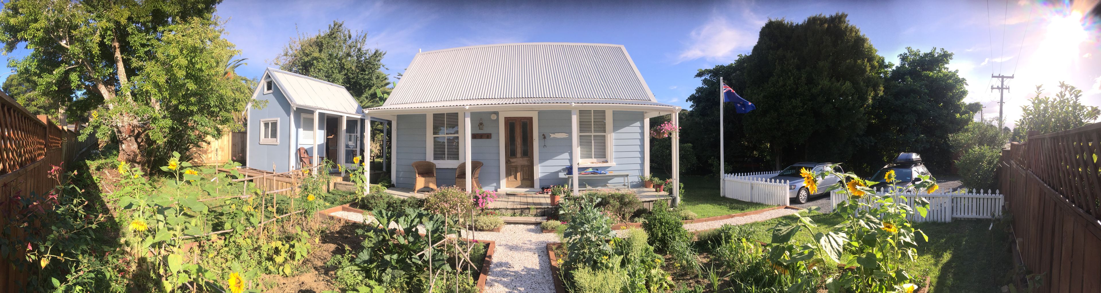 A house with a porch, a garden with sunflowers, and a flag.