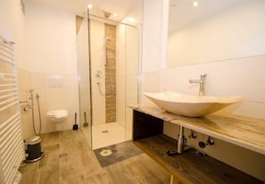 Een moderne badkamer met een douche met glazen wand, een grote wastafel en een houten wastafelmeubel.