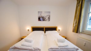 A double bed with neatly folded white towels, a headboard, bedside lamps, and a framed picture on the wall. - Apartment Summer & Winter Fun I (Zell am See)