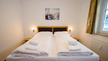 A double bed with white linens and towels, a wooden headboard, bedside lamps, and a framed picture on the wall.