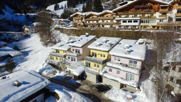 A snow-covered residential area with multi-story buildings, including a hotel with balconies and a ski resort in the background.