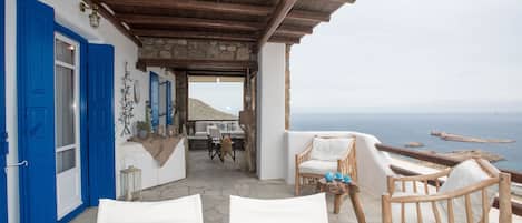 Una terraza costera con muro de piedra, puertas azules y mobiliario blanco.