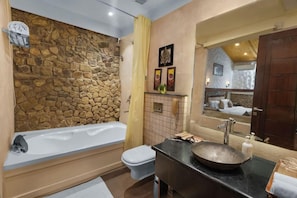A bathroom with a stone wall, a bathtub, a toilet, and a sink with a large basin. - Shaantam Resorts (Yamkeshwar)